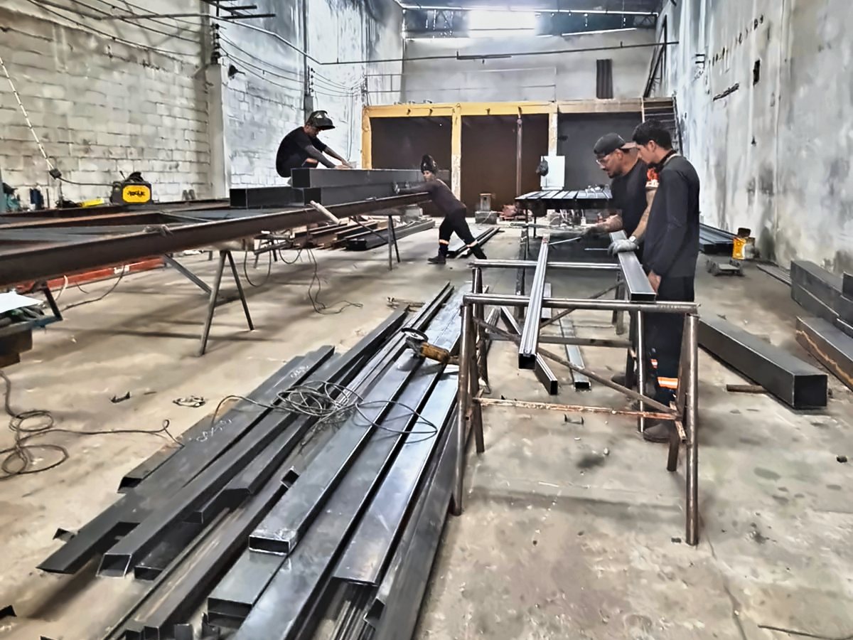 Equipe da Esparta Engenharia cortando e montando perfis metálicos dentro de um galpão